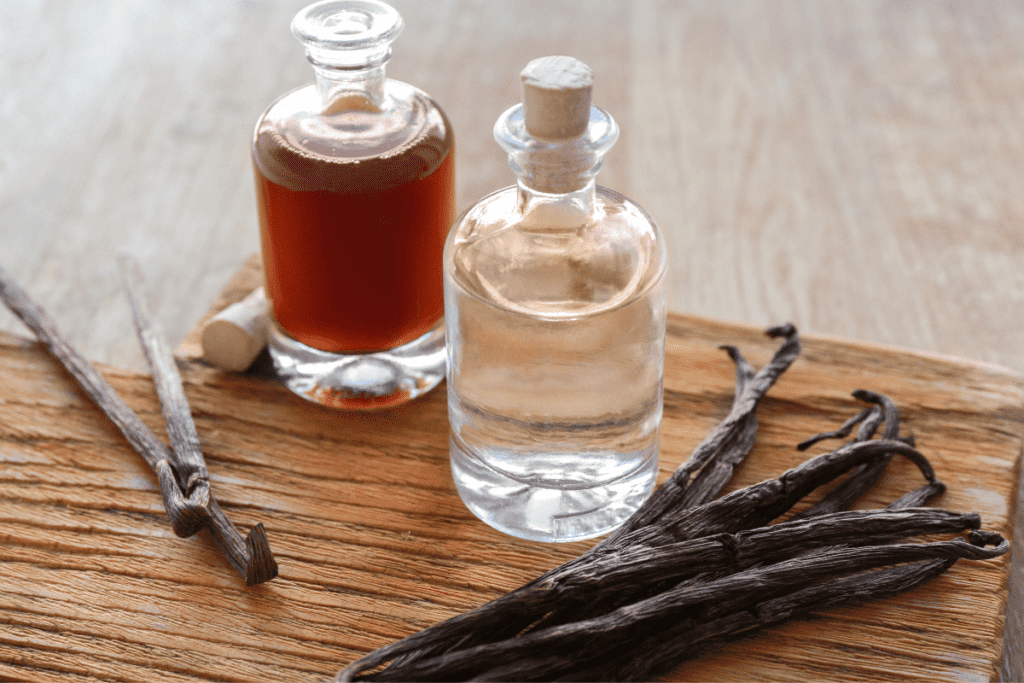 Whole vanilla beans sit on a table alongside some homemade vanilla extract.