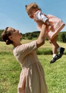 A mom stands in a field holding her baby in the air.