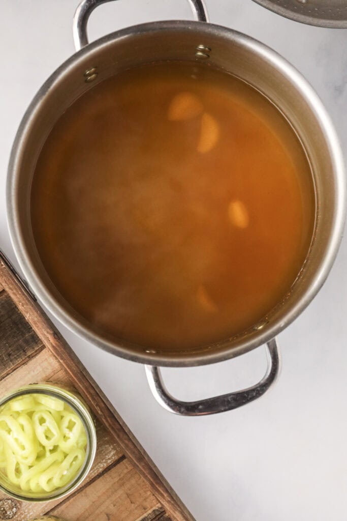 Homemade pickling brine in a pot with vinegar, salt, and garlic cloves for canning banana peppers.