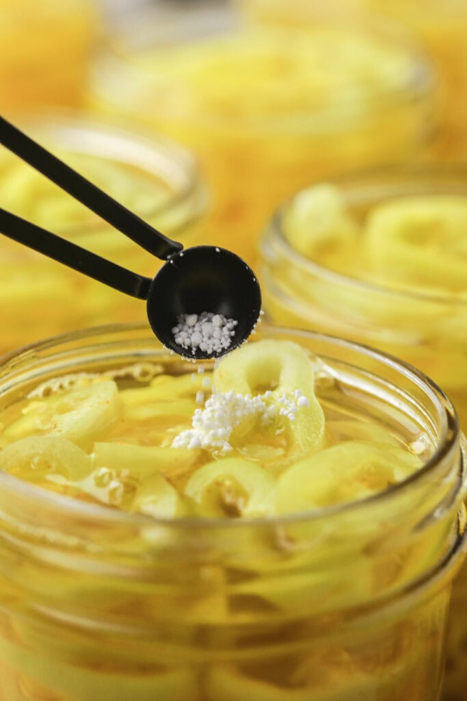Adding pickling crisp to a jar of sliced banana peppers before canning.