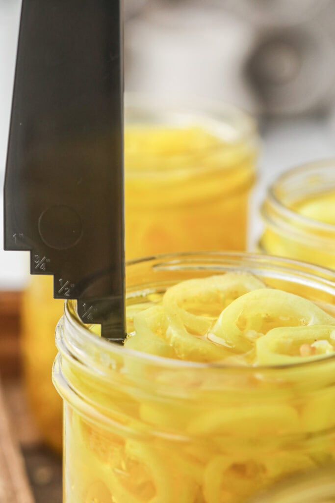 Measuring headspace in a jar of pickled banana pepper rings with a headspace tool before canning.